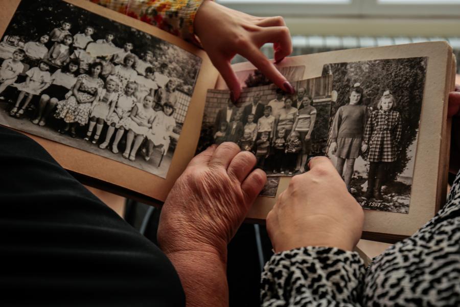 Розгорнутий фотоальбом із чорнобілими фотографіями, руки жінок які тримають альбом і вказують на людей на фото